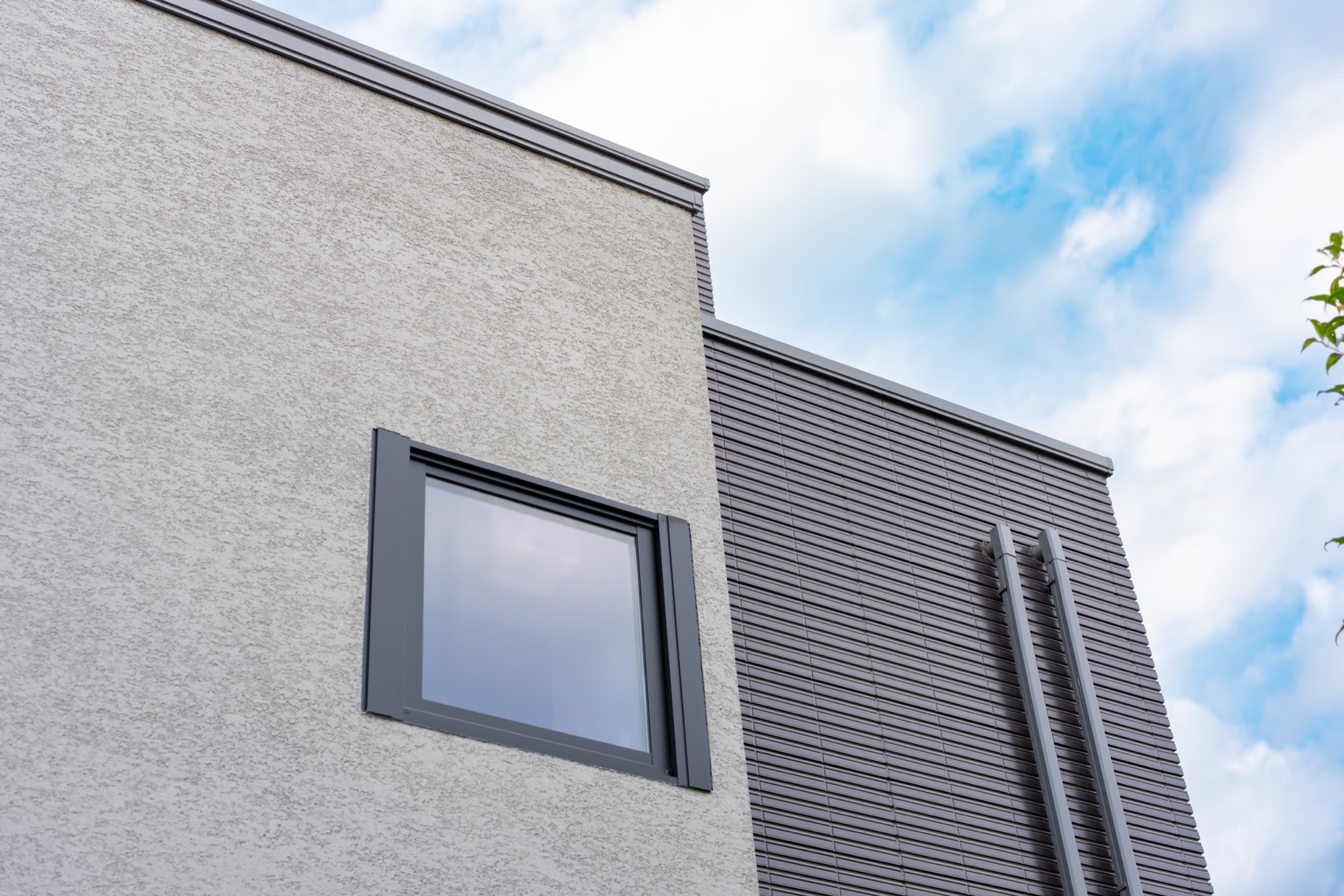 モルタルとチャコールグレーのサイディングのコントラストがモダンな住宅の外壁と青空