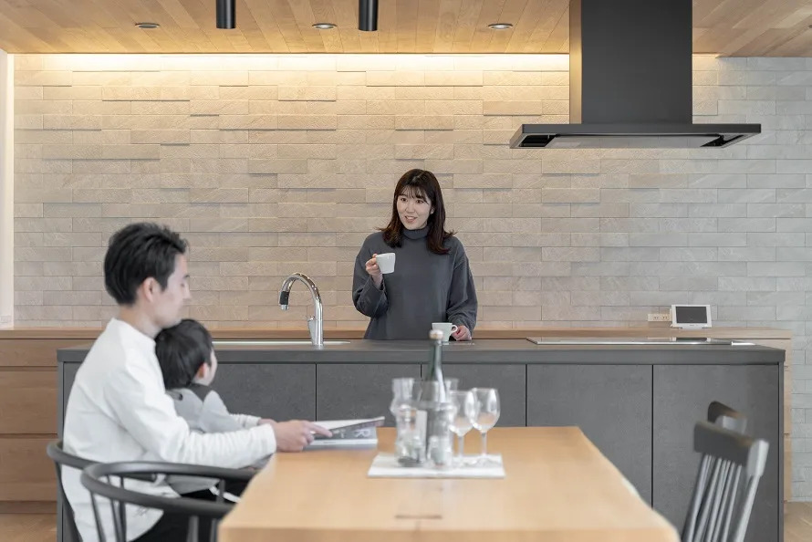 アイランドキッチンの前に立つ母親と会話する、ダイニングテーブルに座る父親の上の男の子