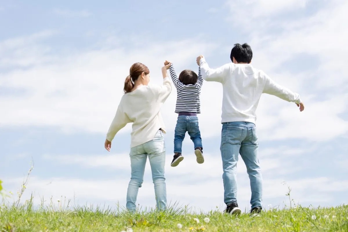 青空の野原で小さな男の子を一緒に持ち上げる、父親と母親