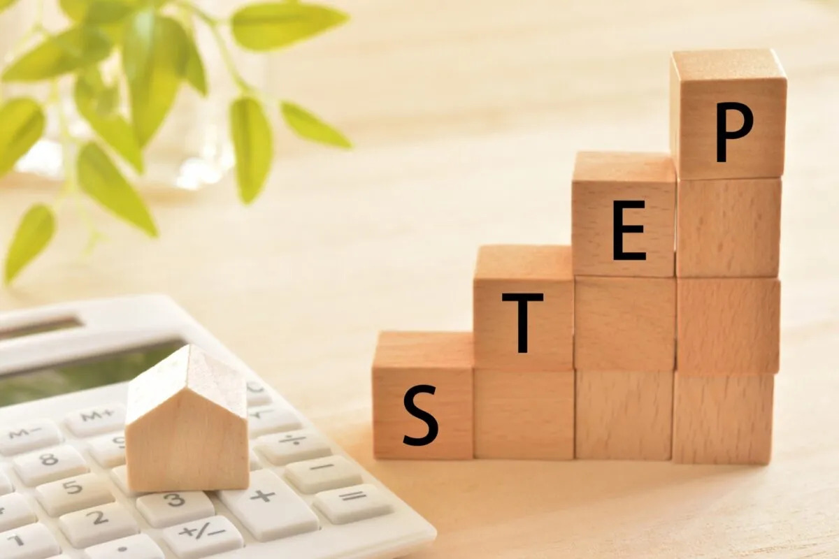 電卓に乗った家型の積み木と、階段上に積み上げられた「STEP」の文字が入った木のブロック