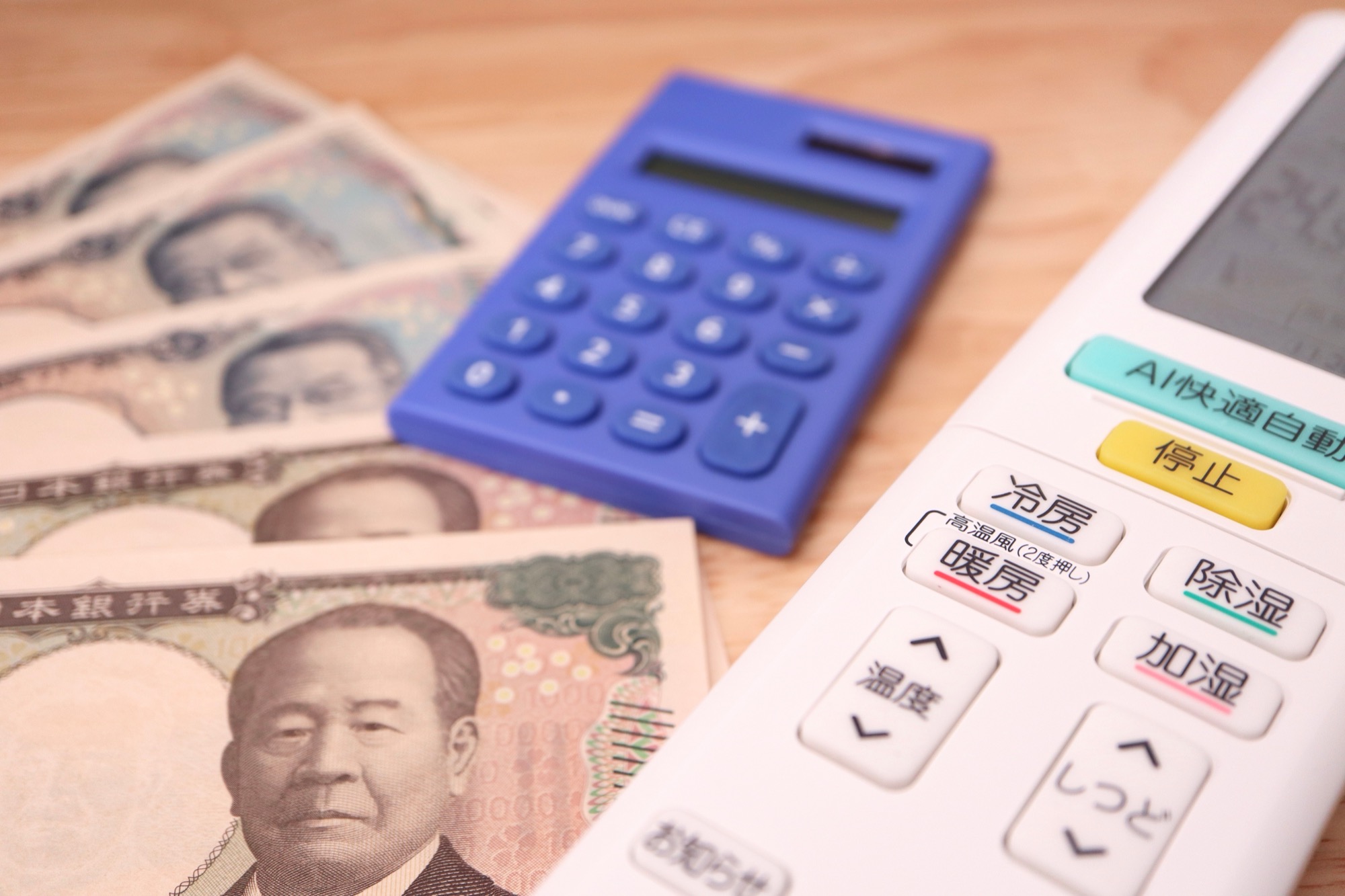 エアコンのリモコン、現金、電卓で表した光熱費節約のイメージ