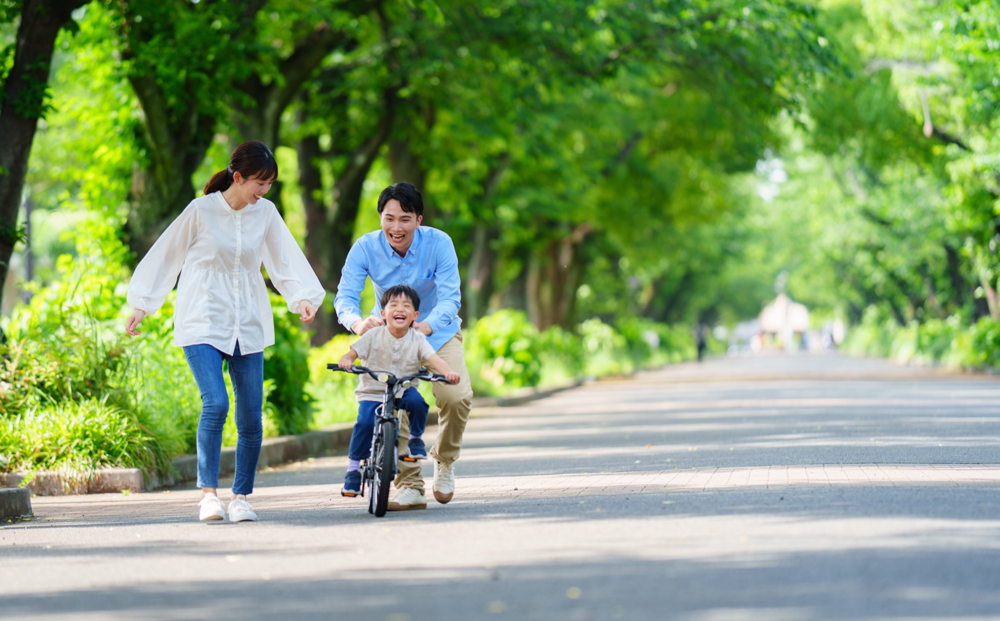 緑道の中で自転車を練習する男の子と両親