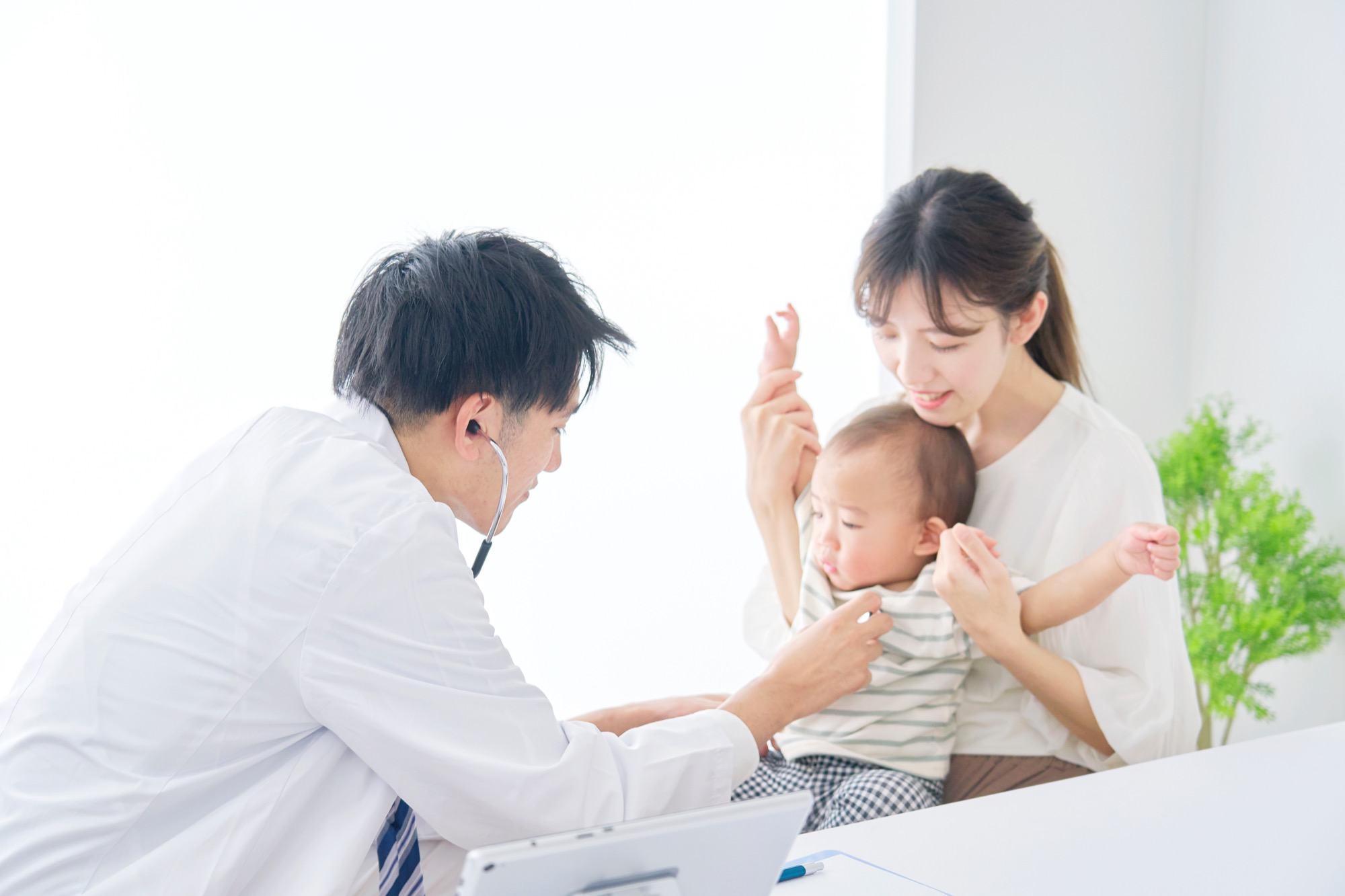 母親の膝の上にいる赤ちゃんの診療を行う小児科の医師