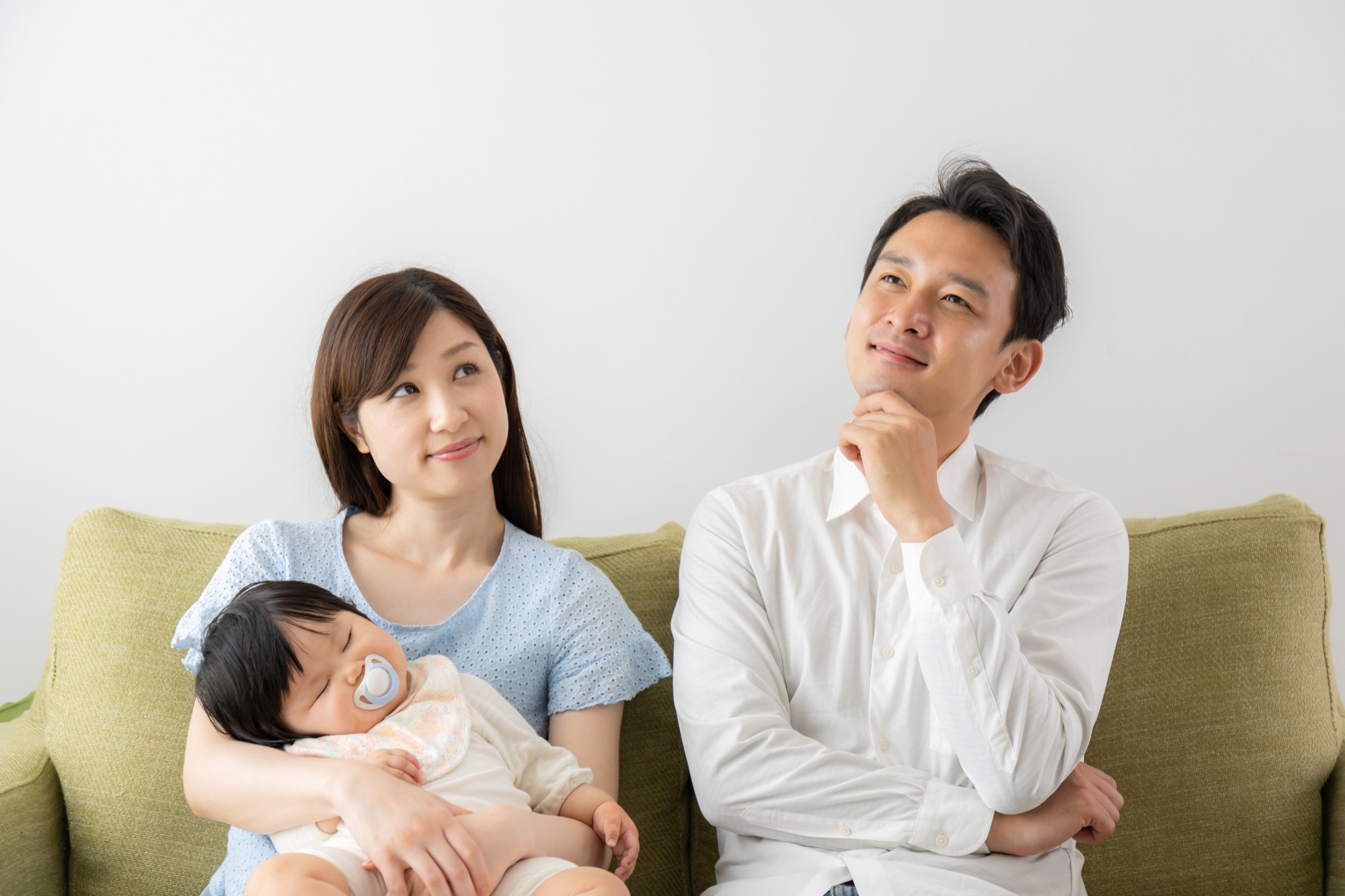 子育ての疑問に首を傾げる、眠った赤ちゃんを抱っこする母親と父親