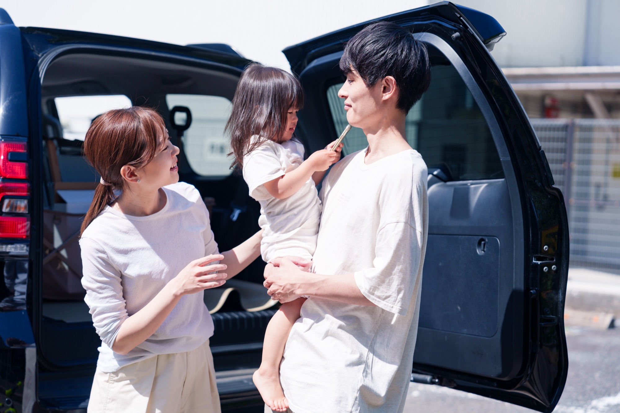 車でお出かけする若い夫婦と小さな女の子の3人家族