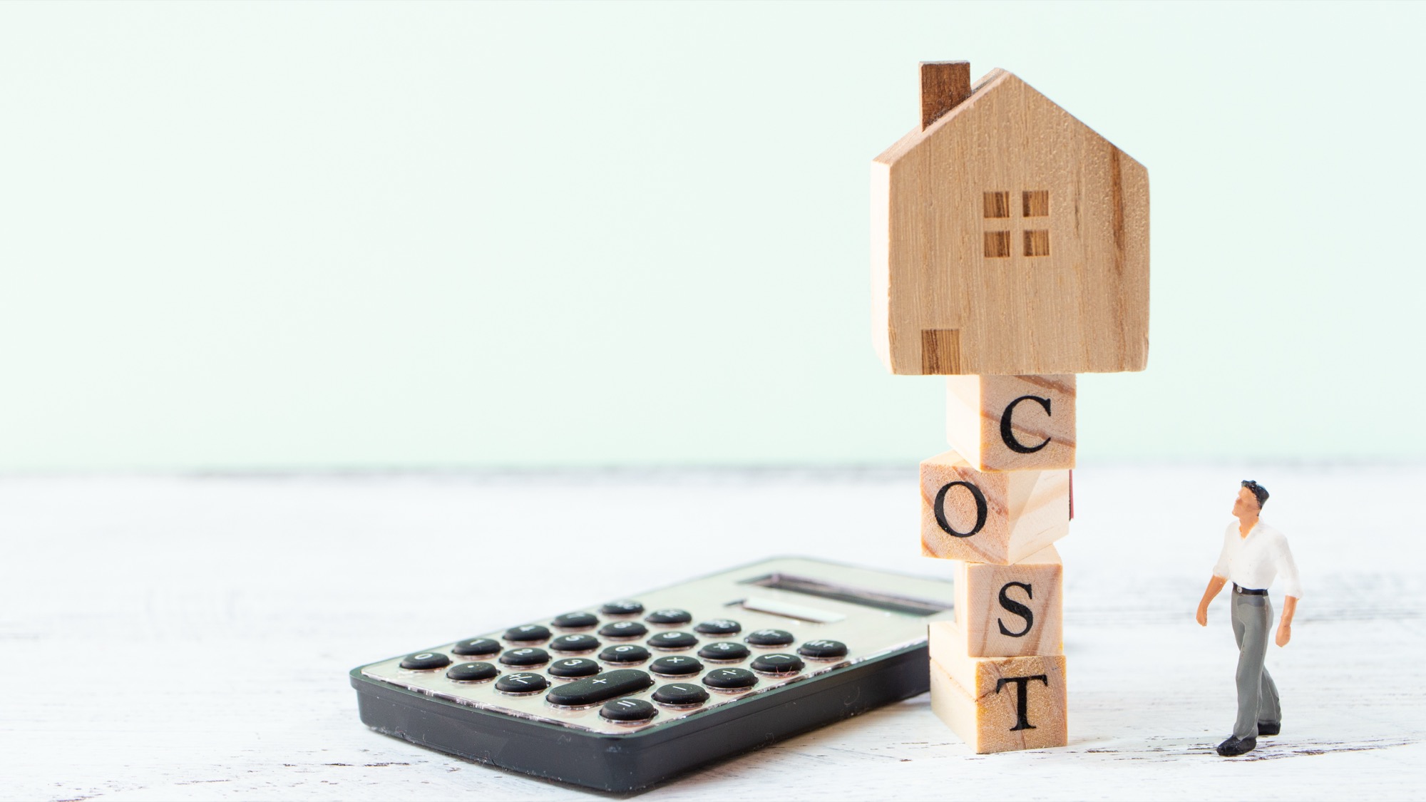 COSTと書かれた木のブロックと木の模型、電卓、人の模型