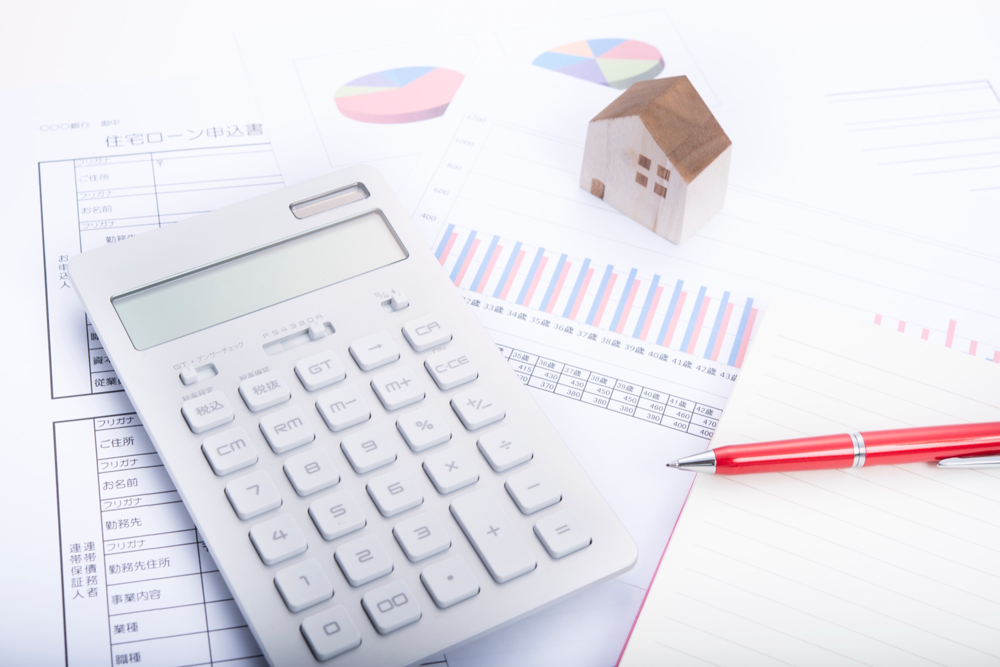 住宅ローンの検討資料と電卓、木の住宅模型