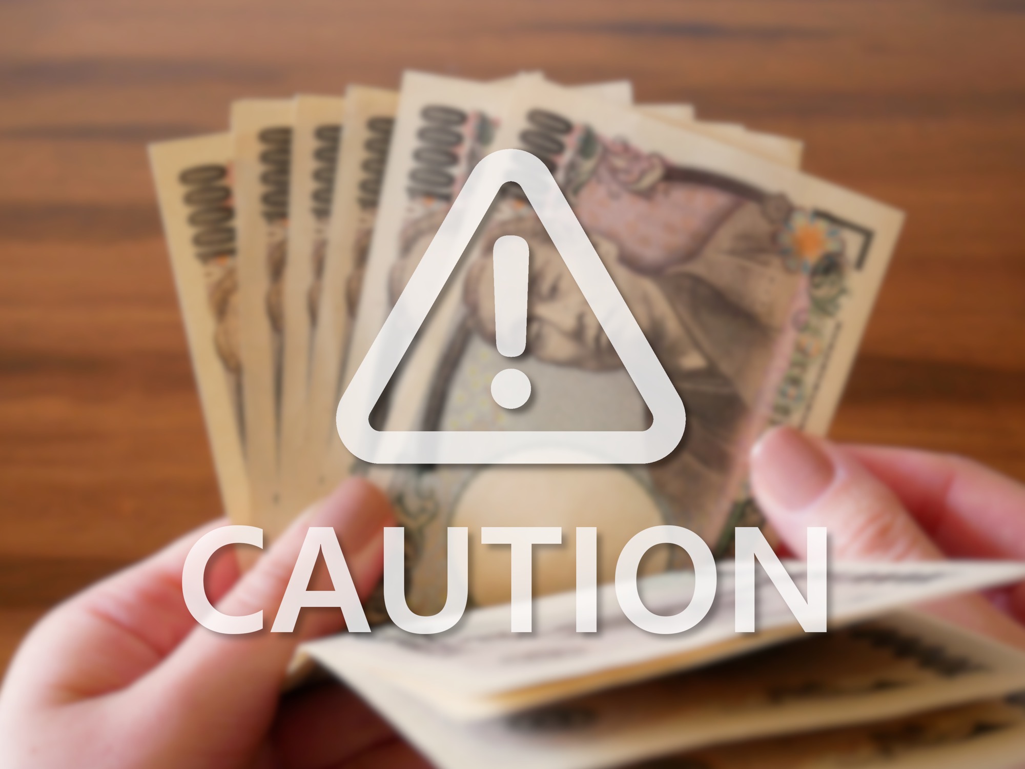 1万円札を数える女性の手をバックに書かれた「CAUTION」の文字