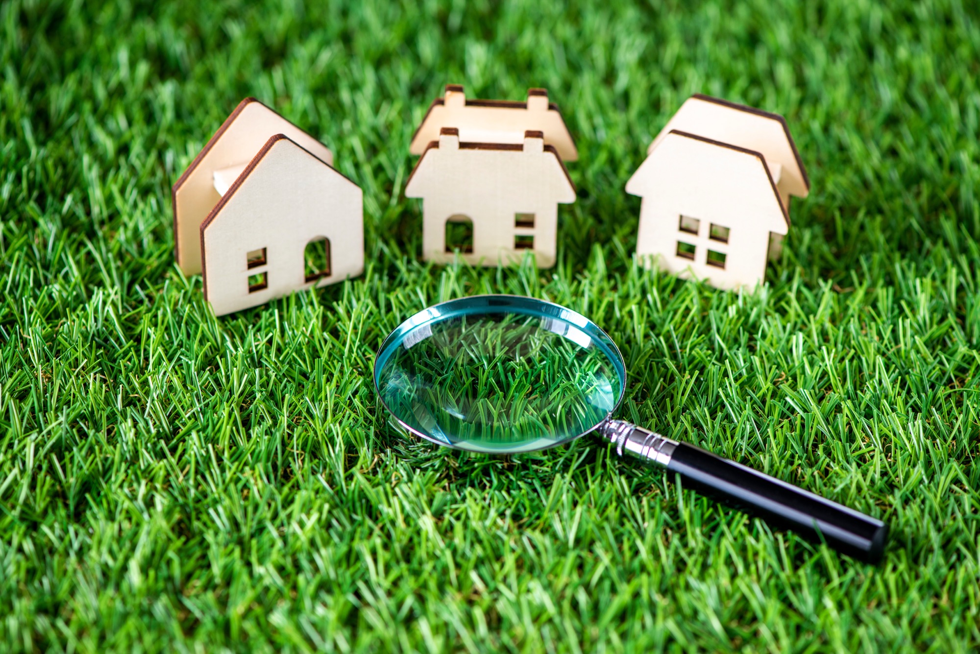 芝生の上に置かれた虫眼鏡と3つの住宅模型